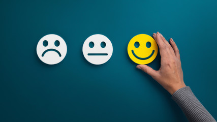 Woman choosing happy smiley face emotion on blue