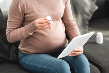 cropped view of pregnant woman holding pills while having online consultation with doctor on digital tablet