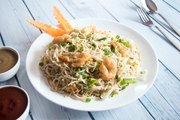 Chicken noodles on a white plate placed on a wooden board.
