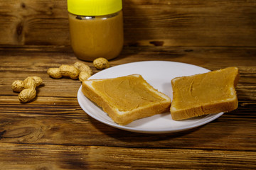 Jar of peanut butter and plate with two sandwiches with peanut butter on wooden table
