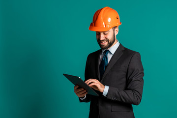 Young engineer businessman in suit jacket makes notes on tablet about building project, report. Businessman isolated on blue background as on construction. He is satisfied.