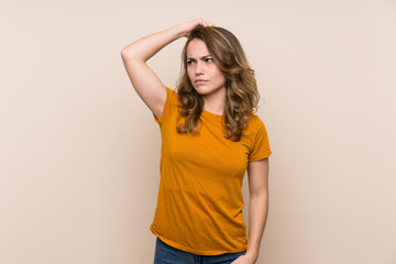 Young blonde girl over isolated background having doubts while scratching head