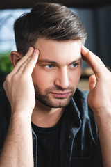 handsome man with headache touching head and looking away in apartment