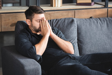 Fototapeta na wymiar man with headache sitting on sofa and obscuring face in apartment