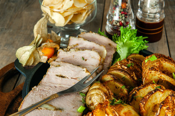 A piece of baked stuffed meat with potatoes and vegetables in a frying pan and a wooden Board