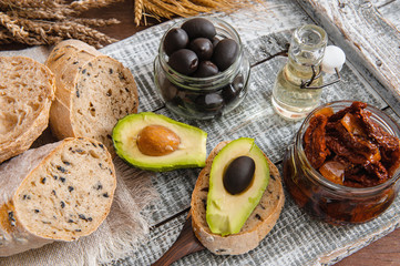 Healthy rye wholegrain bread with olives, avocado and sun-dried tomatoes on a wooden farmer's table. Homemade cake. traditional Italian food