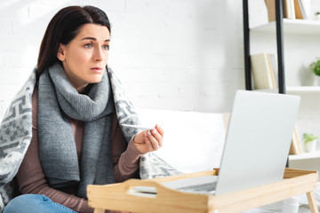 cold woman with thermometer having online consultation with doctor on laptop