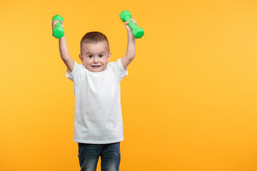 Boy liftimg dumpbells over his head. He is standing over yellow background