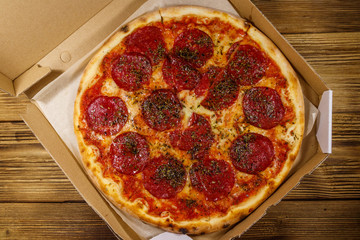 Delicious fresh pizza in cardboard box on a wooden table. Top view. Concept for home delivery of food, fast food, delivery of pizza