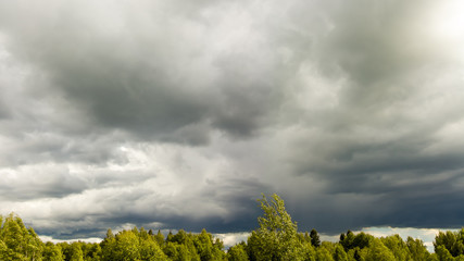 Landscape with dark storm clouds over the green tops of trees