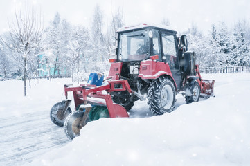 A red old tractor clears the street of snow in a snow storm. Street cleaning in winter