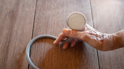 Old hand holding stethoscope on a wooden floor. Concept Old age health care plan.