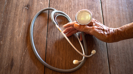 Old hand holding stethoscope on a wooden floor. Concept Old age health care plan.