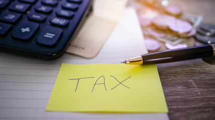 On the desk have coin pile, calculator,   account book and Note paper have tax on it. Concept Planning for spending and accumulating money Including paying taxes.