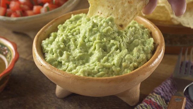 Hand dipping a nacho chip into a bowl of freshly made guacamole.