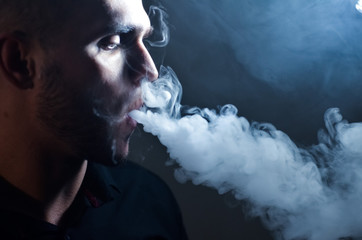Man vaping e-cigarette with e-liquid, close-up, breathes out large cloud of steam or vapor. Vape...