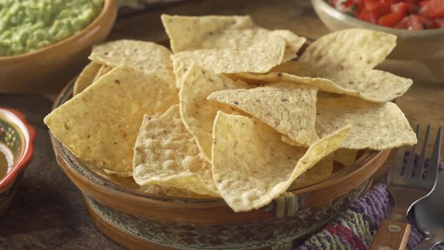 A basket of delcious tortilla chips on a rustic wood table top.