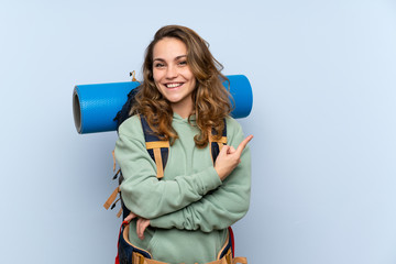 Young blonde hiker girl over isolated blue background pointing to the side to present a product