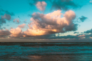 Fototapeta na wymiar Ostseestrand mit Wellen, Gischt bei Sonnenuntergang mit rotgelb leuchtenden Wolken im Winter