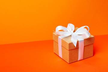 Trendy attractive minimalistic gift on the orange background. Merry Christmas, St. Valentine's Day, Happy Birthday and other holidays concept. Copy space.