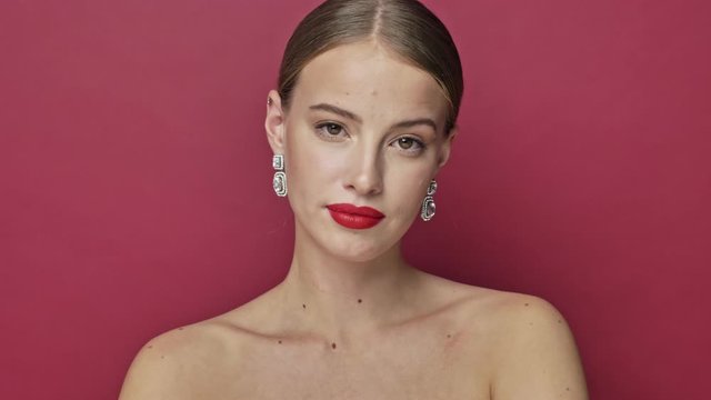 Serious young woman with red lipstick and earrings is showing a middle finger isolated over red background