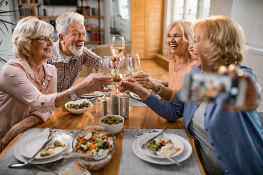 Group Of Happy Seniors Toasting With Wine While Taking Selfie At Dining Table.