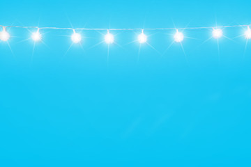 Christmas ornaments on cyan blue background. Festive decorations, white sparkling and glowing lights garland. Traditional winter holiday celebration accessories. Xmas backdrop with copyspace