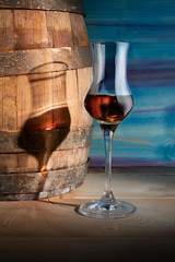 A glass of whiskey next to an oak barrel on a blue background