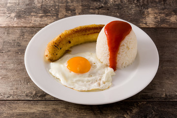 Arroz a la cubana Typical Cuban rice with fried banana and fried egg on a plate on wooden table