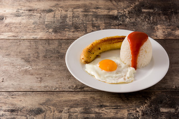 Arroz a la cubana Typical Cuban rice with fried banana and fried egg on a plate on wooden table copy space