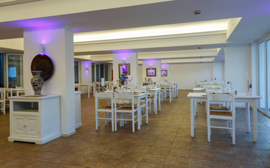 evening interior of the restaurant with white furniture and tables in resort European hotel, Greece