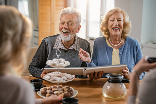 Cheerful mature couple looking at photo album and talking to their friends at home.