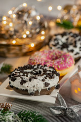 Pink and chocolate doughnuts lie on the Christmas table next to a candlestick. New year celebration