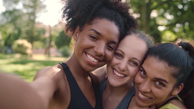 Smiling portrait of happy diverse female friends looking at the camera taking a selfie in the park and laughing