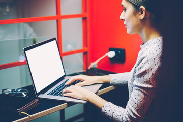 Serious female manager typing on laptop computer with mock up screen making preparation for making...