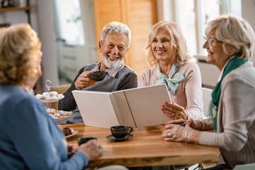 Obraz premium Happy mature friends talking about their memories while looking at photo album at home.