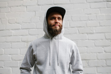 City portrait of handsome hipster guy with beard wearing gray blank hoodie or sweatshirt and cap...