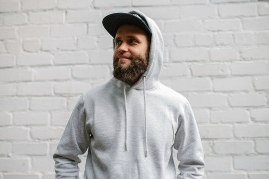 City portrait of handsome hipster guy with beard wearing gray blank hoodie or sweatshirt and cap with space for your logo or design. Mockup for print