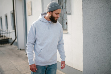 City portrait of handsome hipster guy with beard wearing gray blank hoodie or sweatshirt with space...
