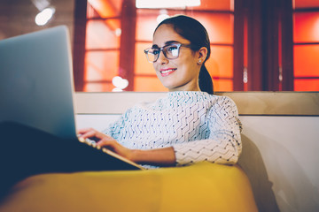 Smiling woman watching video on laptop computer working on freelance in cozy coworking interior,female student resting during free time reading news blogging in social networks using netbook