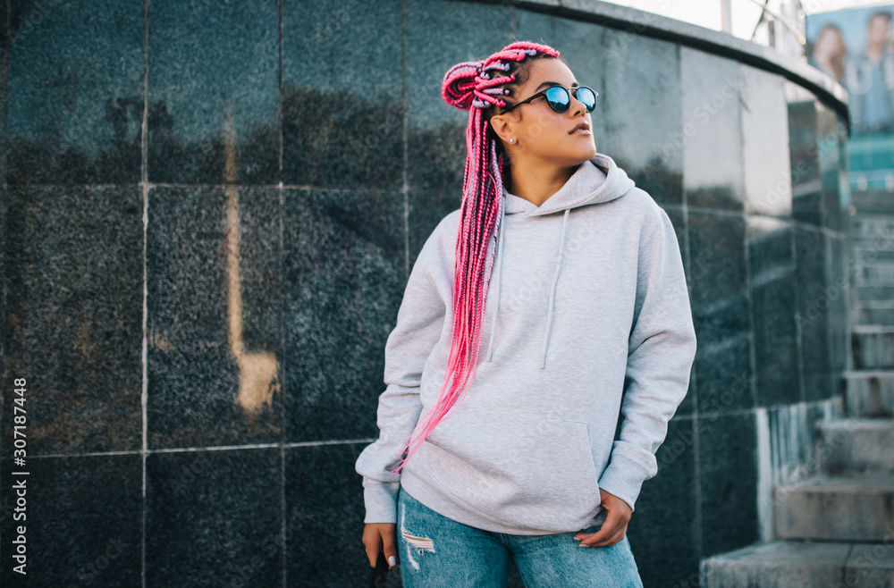 Wall mural City portrait of handsome hipster girl with colored afro braids wearing gray blank hoodie or hoody with space for your logo or design. Mockup for print - Wall murals