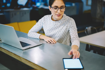 Businesswoman in eyewear checking notification on touchpad with blank screen synchronize files with...