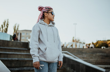 City portrait of handsome hipster girl with colored afro braids wearing gray blank hoodie or hoody with space for your logo or design. Mockup for print