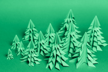 Several paper Christmas trees made using the origami technique on a green paper background. Forest conservation concept