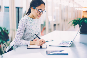 Concentrated female administrative manager copying information from web page on laptop computer...