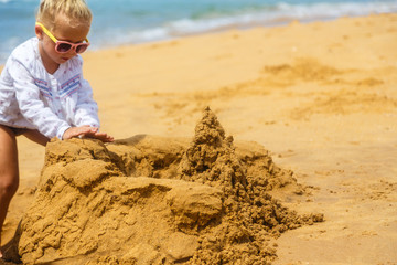 little girl in sunglasses builds sand castle on the ocean shore