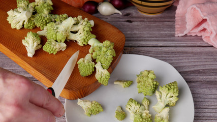 Female hand with a knife discards pieces of Roman cauliflower Romanesco from a cutting board into a plate. Sliced Roman Cauliflower
