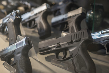 Black pistols behind the glass of a weapon store counter. Unusual look