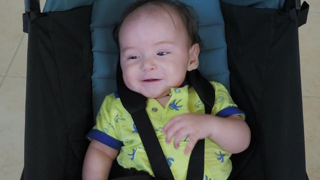 Little cute smiling child sits in a pram and laughs. Joyful funny boy in foldable baby stroller. Happy childhood and motherhood concept.