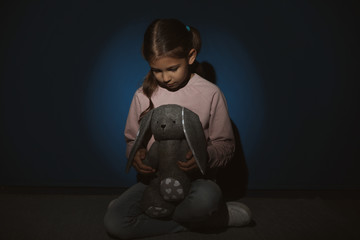 Sad little girl with toy near blue wall. Domestic violence concept